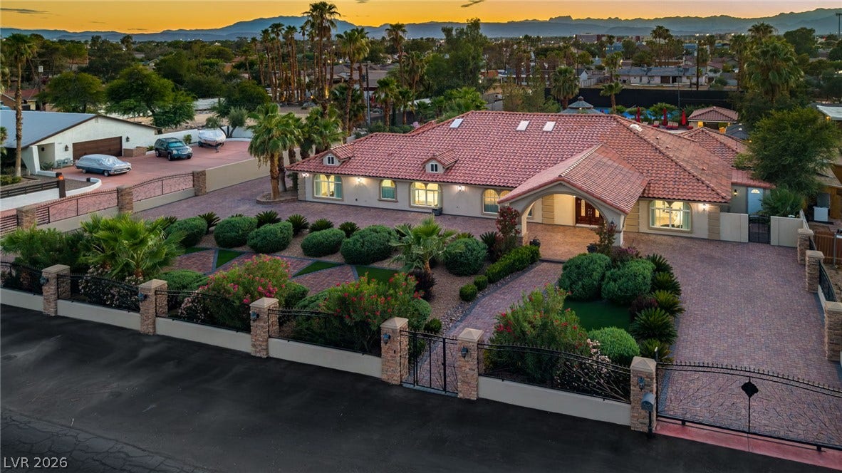 1355 Westwind Road, Las Vegas, NV 89146 Gated desert estate showcasing an expansive paver driveway and a classic tile roof under twilight skies.