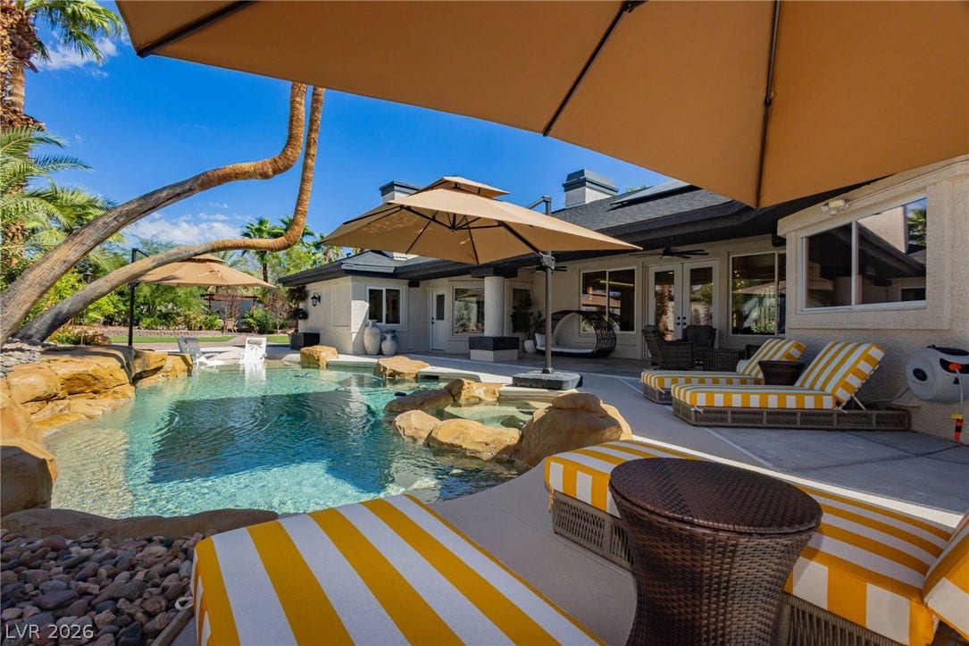 A customized rock-rimmed pool with an integrated spa highlights the spacious backyard concrete patio.