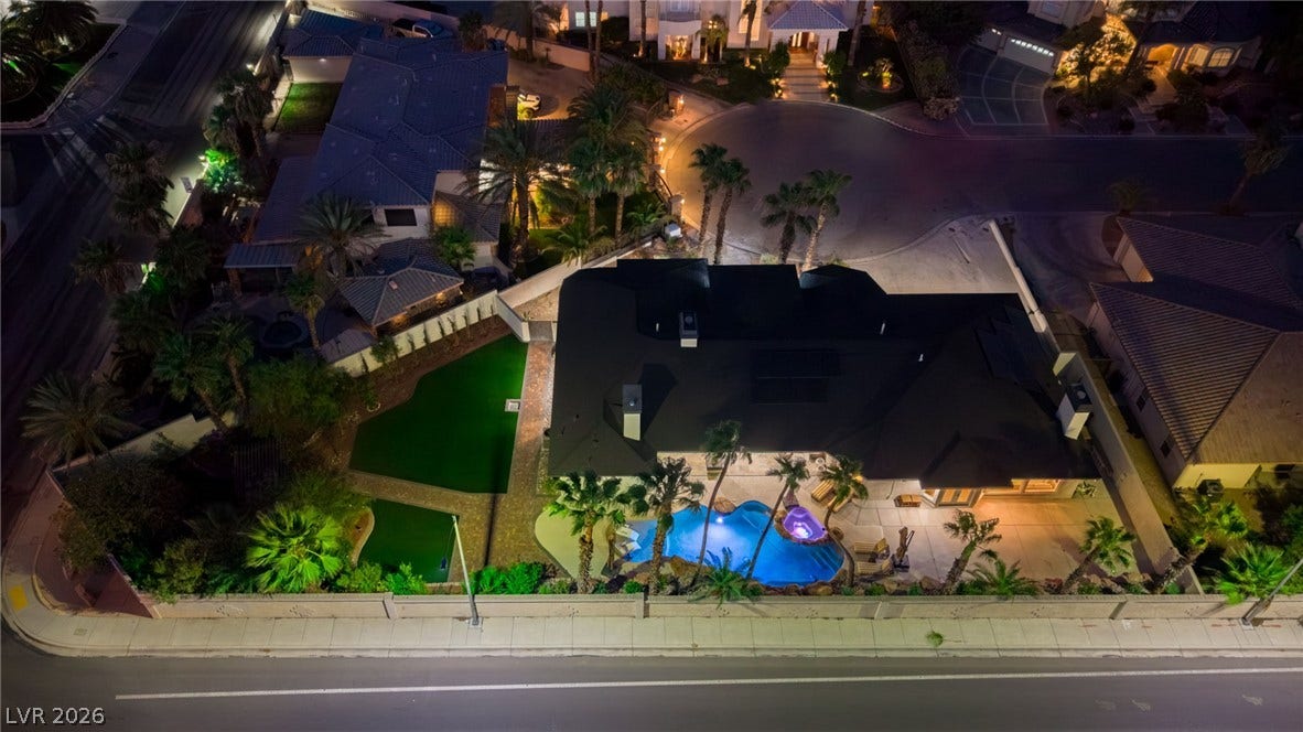 An illuminated backyard pool highlights this aerial night perspective of the estate.