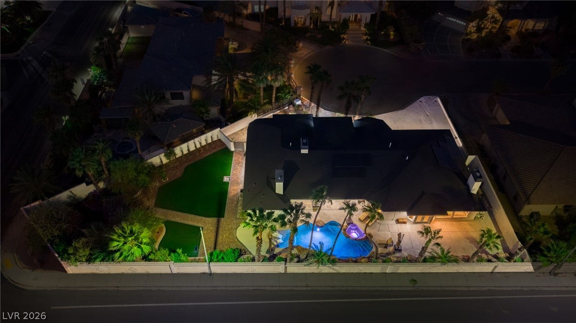 Dramatic night illumination highlights this impressive property featuring a sparkling pool, manicured lawns, and palm-fringed landscaping.