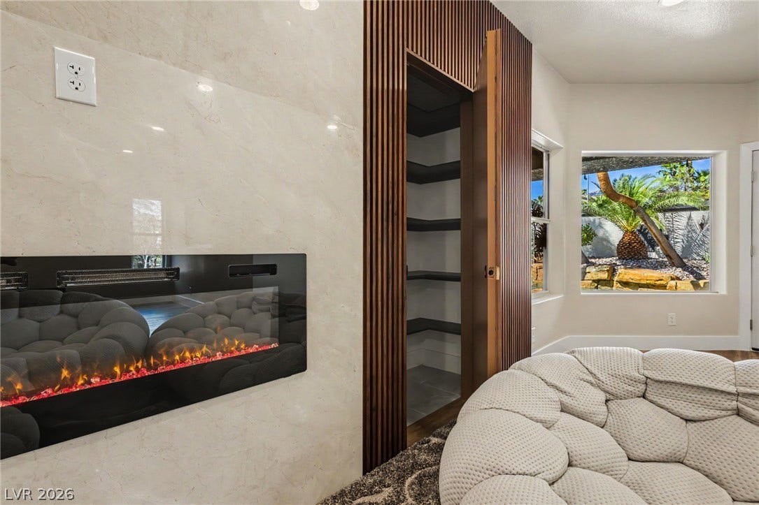 Polished tile surrounds a modern electric fireplace, adjacent to a hidden wood-paneled closet.