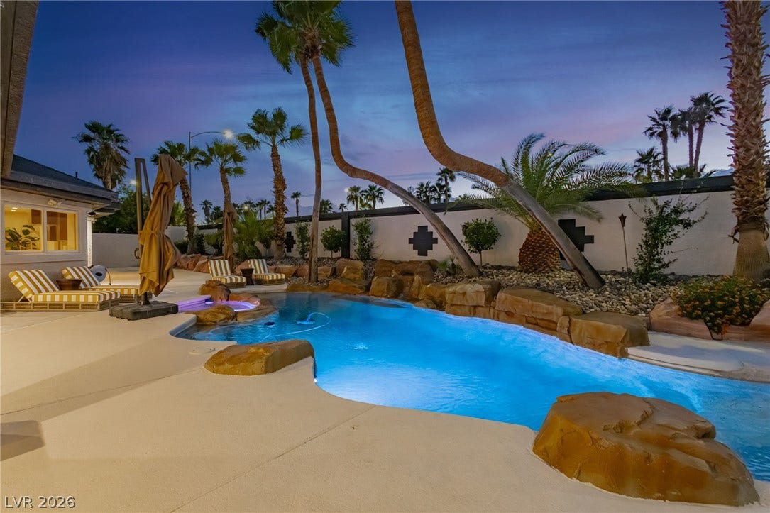 Lush palm trees and custom rock features border a glowing in-ground swimming pool.