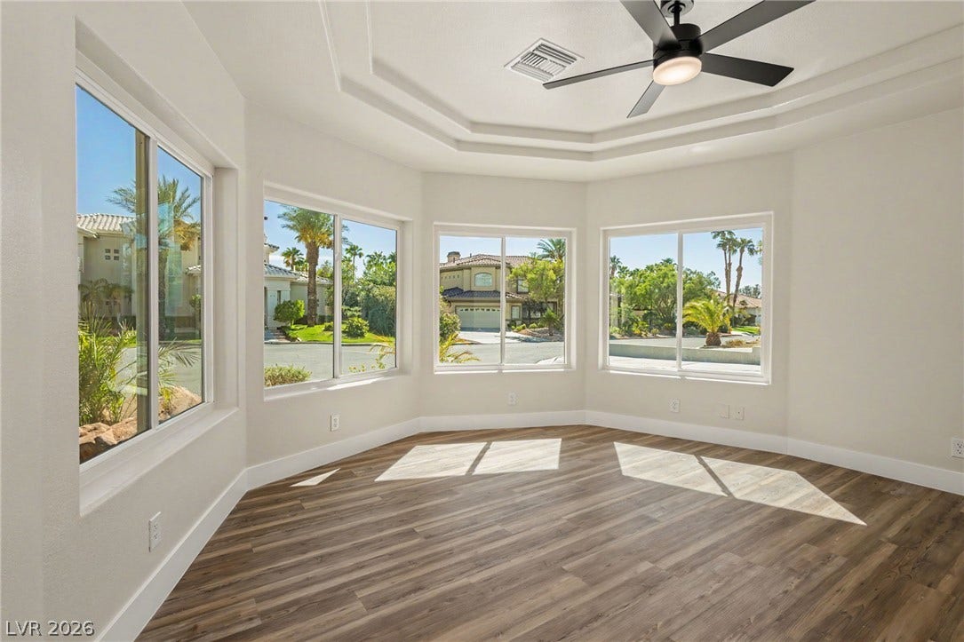 Multi-tiered tray ceilings and rich wood-look flooring define this sun-drenched architectural space.