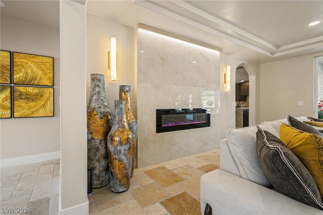 A modern electric fireplace set in a polished stone surround grounds this open living space.