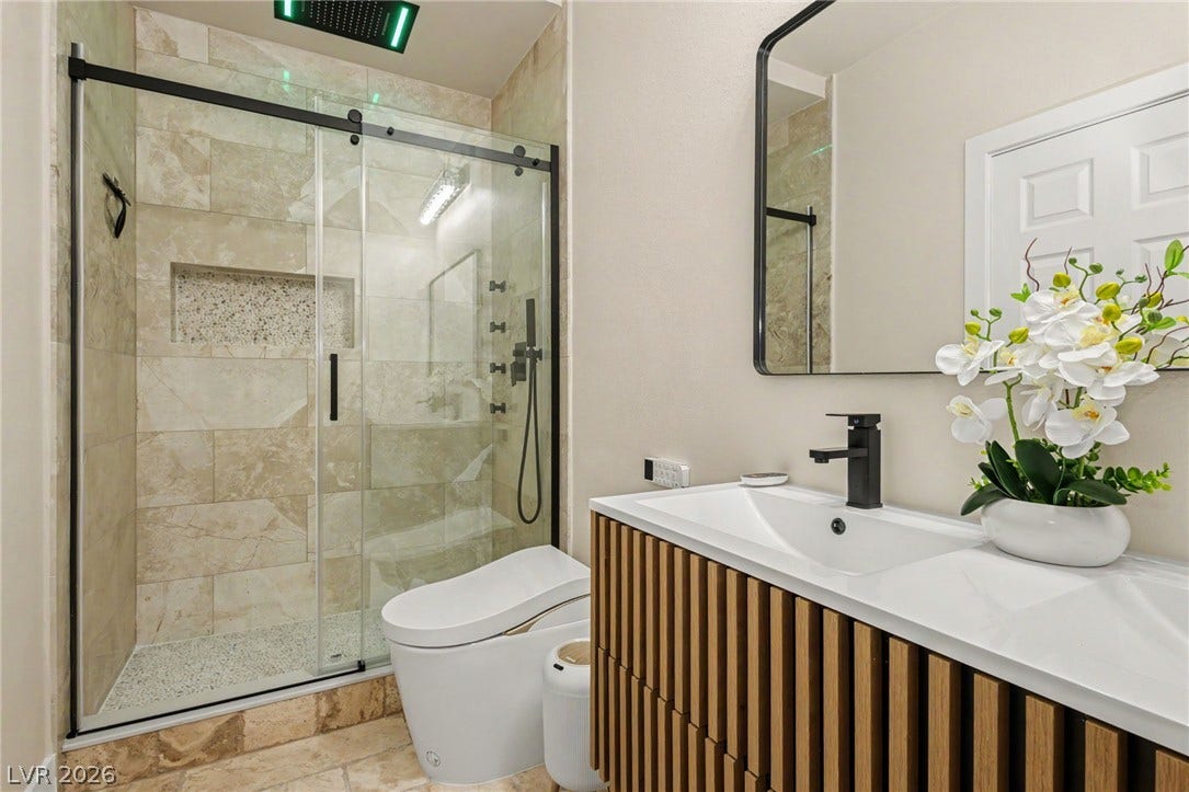 An elegant glass-enclosed walk-in shower anchors this modern bathroom with a contemporary wood vanity.