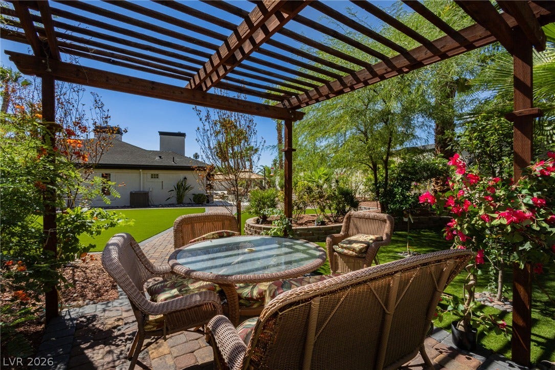 An inviting stone patio sits nestled beneath a handsome wood pergola in the backyard.