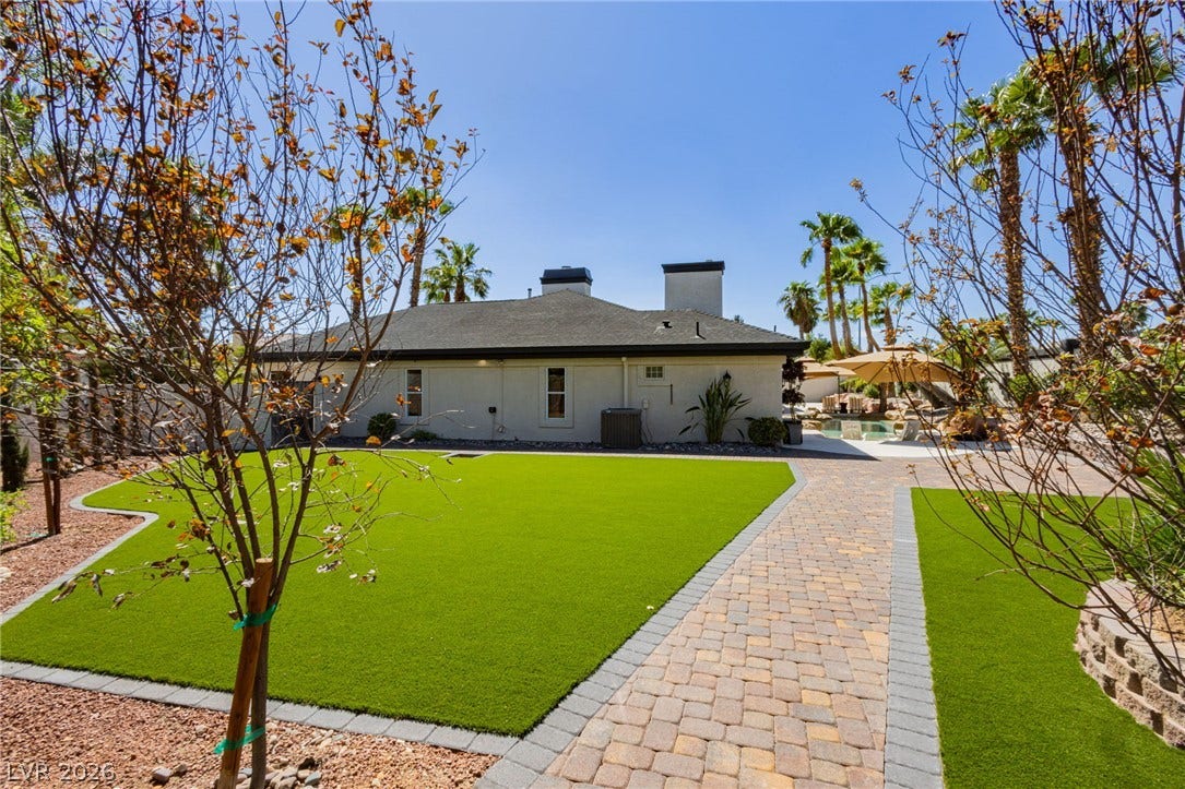 Manicured lawns flank a stone paver path leading toward the backyard pool terrace.
