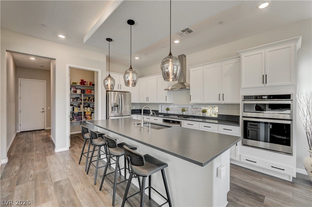 51 Thorn Creek Street, Henderson, NV 89011 Kitchen with stainless steel appliances, a breakfast bar, white cabinets, a kitchen island with sink, and light wood-style flooring