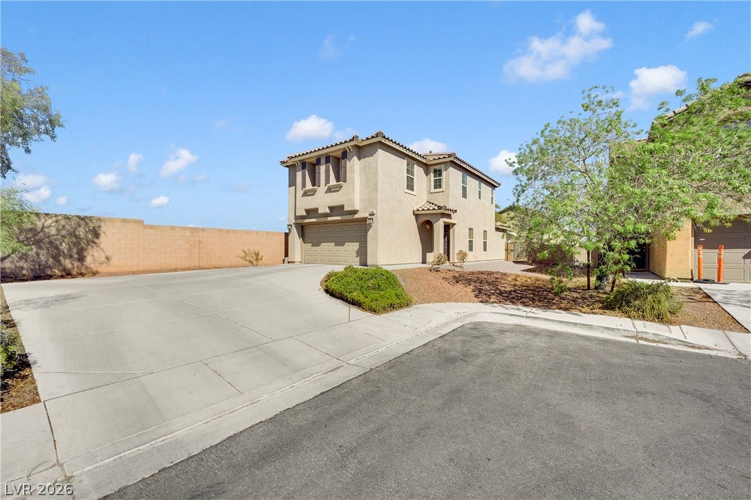 An expansive concrete driveway leads directly to a private two-car garage under clear blue skies.