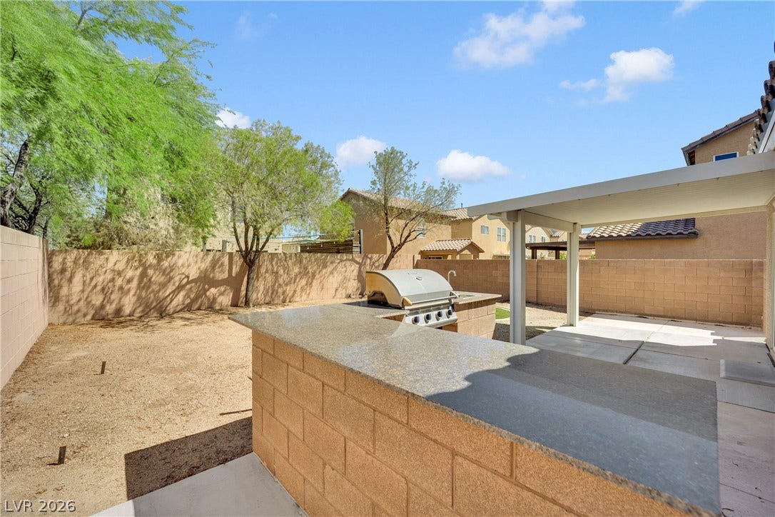 A spacious backyard patio area features a covered concrete pad and a built-in barbecue island.