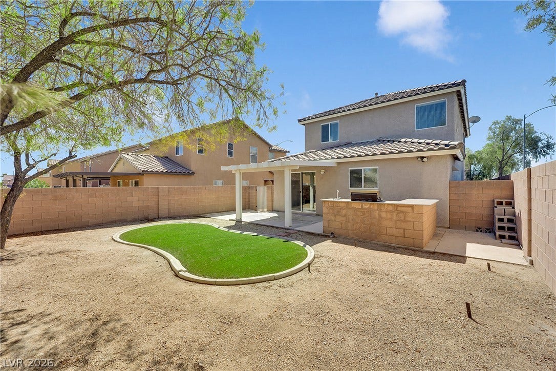 A tiled patio cover, built-in outdoor kitchen, and block wall fencing define the backyard.