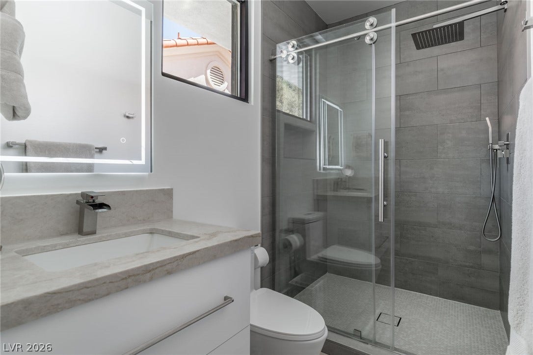 8633 Robinson Ridge Drive, Las Vegas, NV 89117 Clean lines and stone counters highlight this modern washroom featuring a glass-enclosed shower.