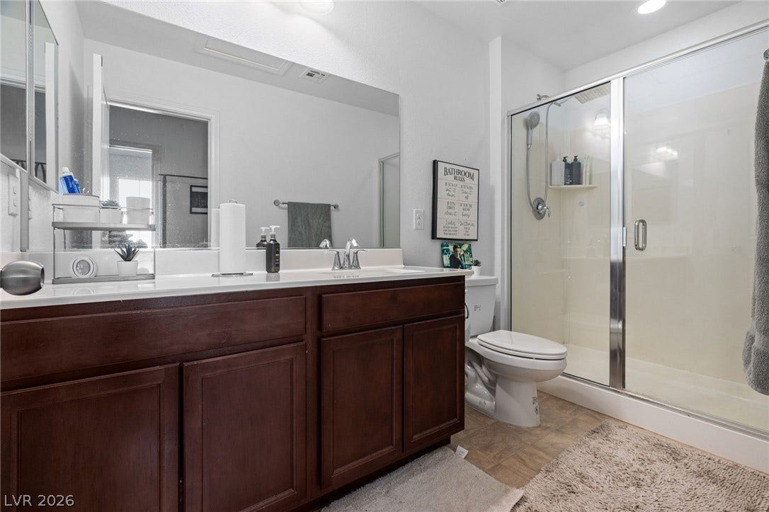 4605 Fragrant Street, North Las Vegas, NV 89031 Rich wood cabinetry anchors this modern bathroom featuring a spacious glass-enclosed shower.