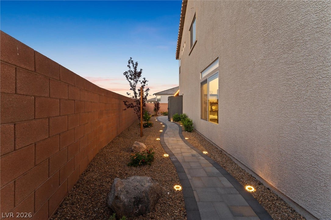 8724 Fortplaid Street, Las Vegas, NV 89139 A beautifully illuminated stone paver path winds alongside the stucco exterior under a twilight sky.