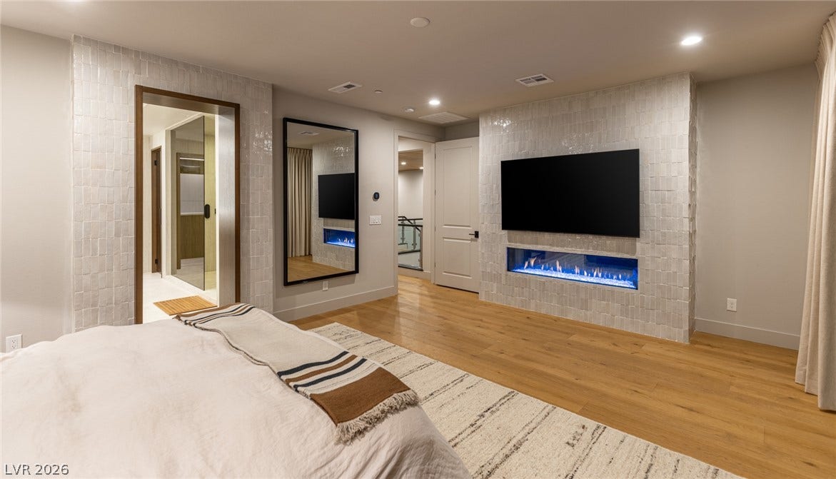 5216 Fading Sunset Drive, Las Vegas, NV 89135 Warm hardwood floors and a modern tiled fireplace define this comfortable main bedroom suite.