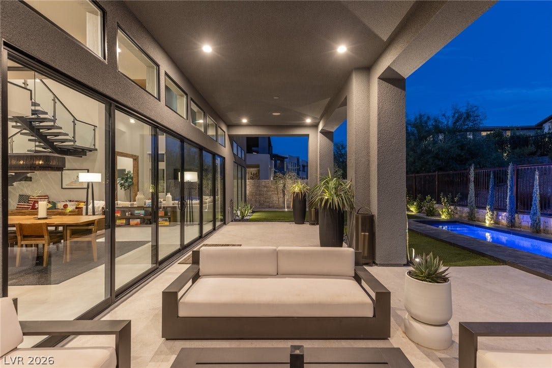 5216 Fading Sunset Drive, Las Vegas, NV 89135 A sleek covered patio with recessed lighting overlooks a narrow, illuminated pool and lush landscaping.