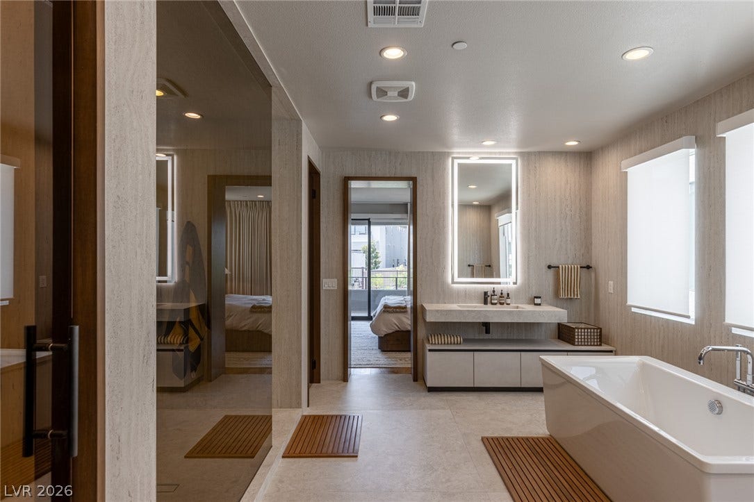 5216 Fading Sunset Drive, Las Vegas, NV 89135 A well-appointed primary bathroom featuring a deep soaking tub and an illuminated vanity, with views into an adjoining bedroom.