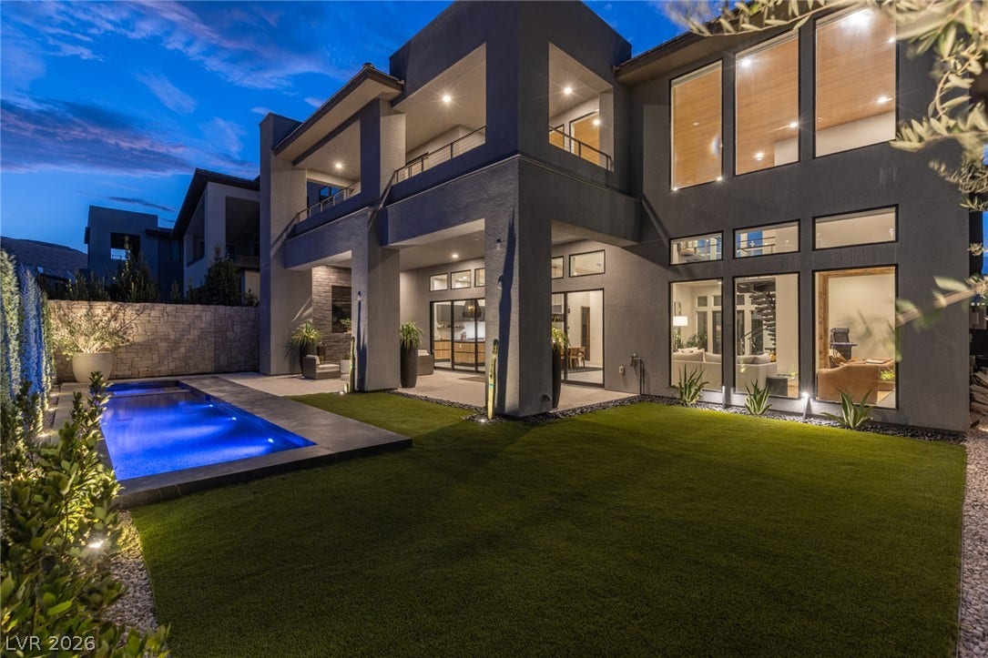 5216 Fading Sunset Drive, Las Vegas, NV 89135 A modern facade with illuminated landscaping and a glowing pool creates a dramatic evening presentation.
