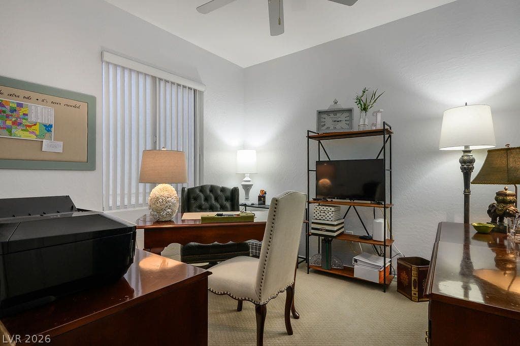 A quiet home office features neutral carpeting and a vertical blind window.