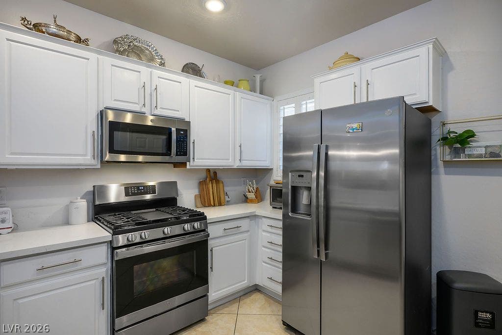 Crisp cabinetry and matching appliances anchor this functional corner kitchen with tile flooring.