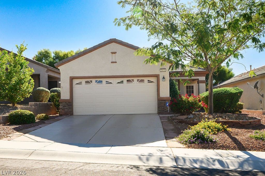 A classic stucco exterior features a concrete driveway and neatly manicured desert landscaping.