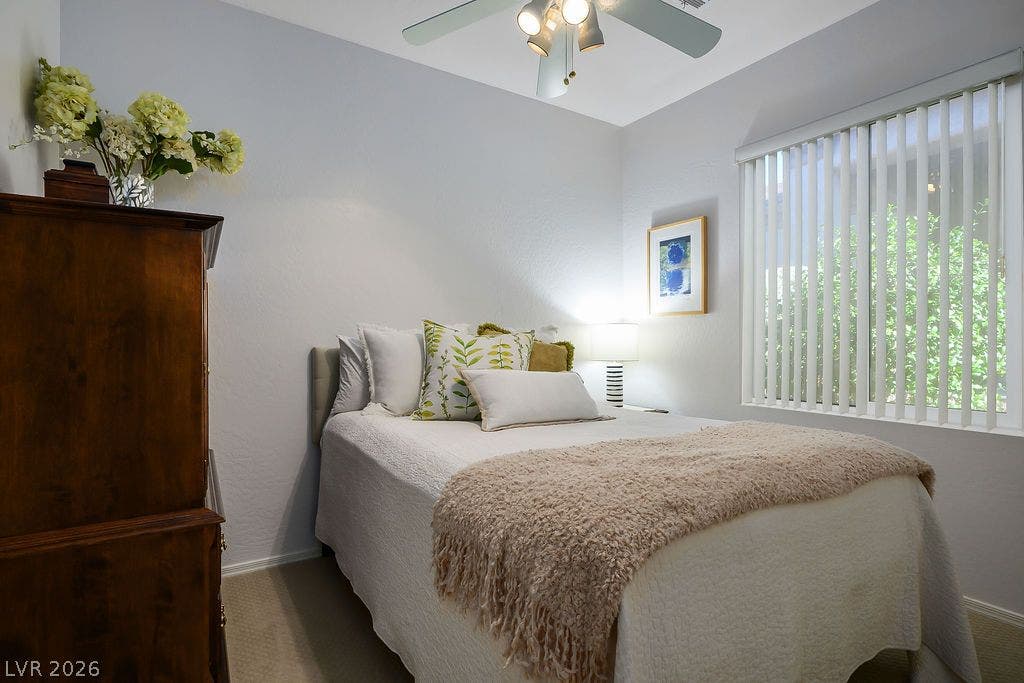 A quiet bedroom offers neutral carpeting and a wide window with integrated vertical blinds.