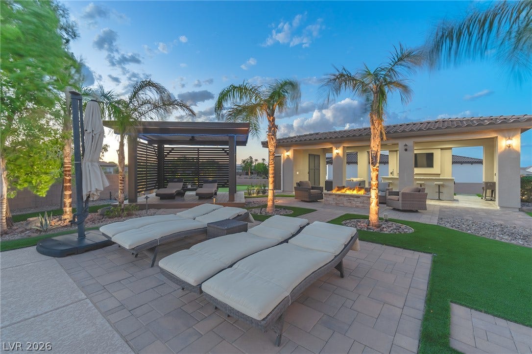 240 San Salvador Avenue, Henderson, NV 89002 An inviting backyard oasis features a paved sun deck, palm trees, and an outdoor kitchen.