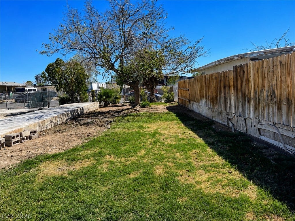 6196 Castlemont Avenue, Las Vegas, NV 89156 Mature trees and a wood fence frame the grassy outdoor space under clear blue skies.