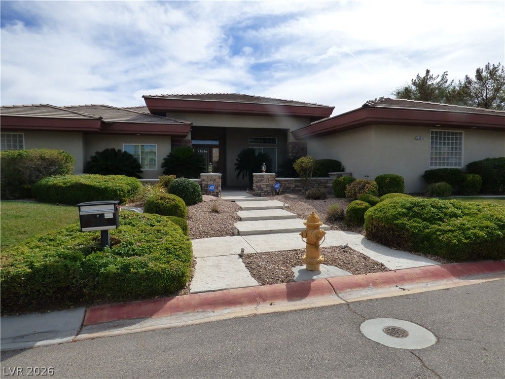 7695 Gilespie Street, Las Vegas, NV 89123 Manicured hedges frame a stone walkway leading to the grand covered entrance of this single-story home.