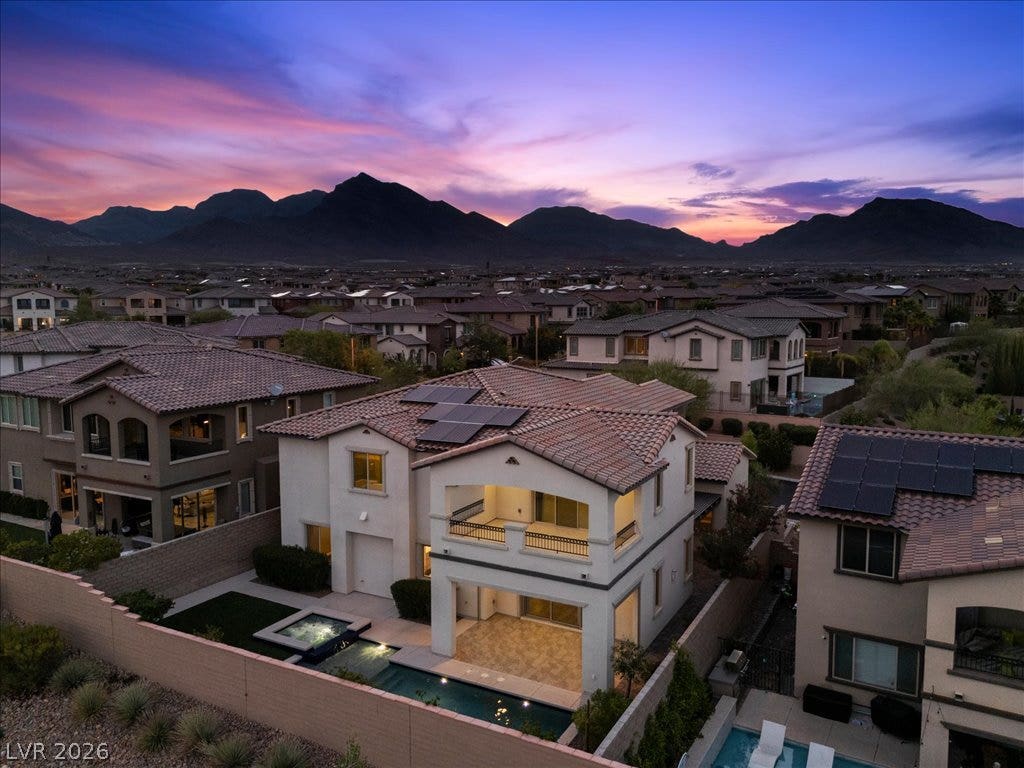 12021 Abbracci Avenue, Las Vegas, NV 89138 An aerial perspective reveals a serene desert oasis, showcasing a residence with a private pool and solar panels, set against a mountainous sunset backdrop.
