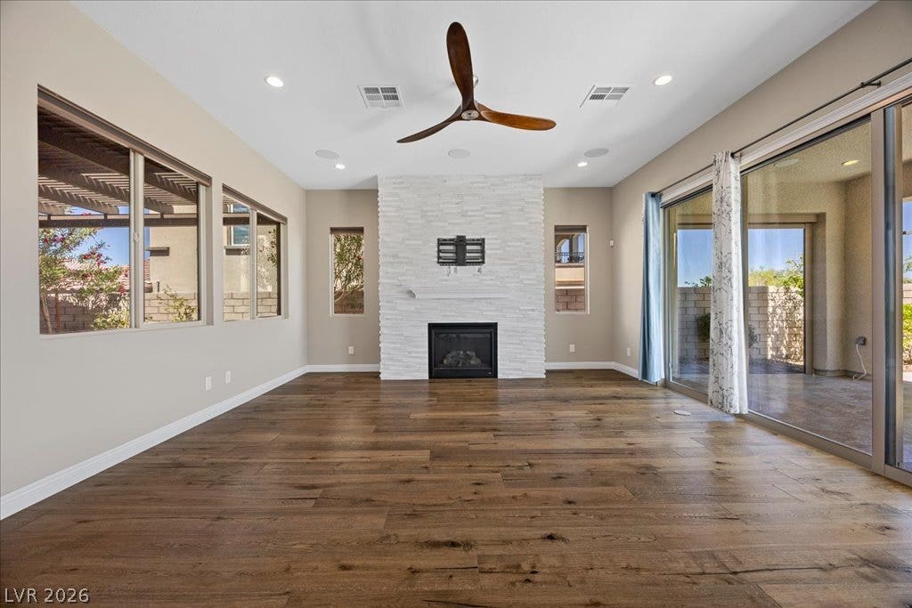 12021 Abbracci Avenue, Las Vegas, NV 89138 A refined living space showcasing a sleek fireplace and rich hardwood flooring, complemented by vast glass doors opening to the outdoors.