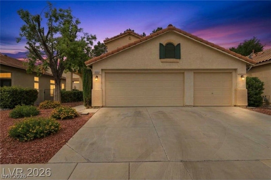 1891 Eagle Flight Lane, Henderson, NV 89012 An expansive concrete driveway leads to a spacious three-car garage set against a desert sunset.