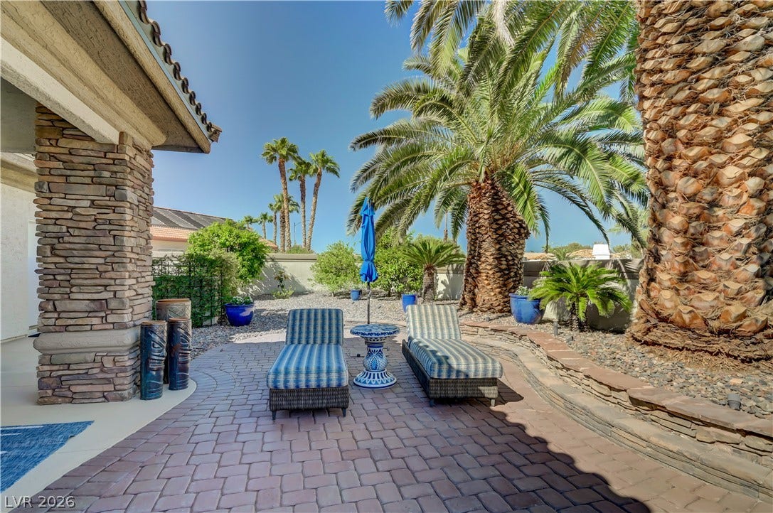 2030 Marina Bay Court, Las Vegas, NV 89117 Lush palm trees and rustic stone pillars frame a paved backyard patio under clear skies.
