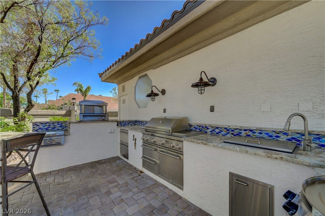 2030 Marina Bay Court, Las Vegas, NV 89117 An outdoor kitchen features premium stone countertops, stainless steel appliances, and a tiled backsplash.
