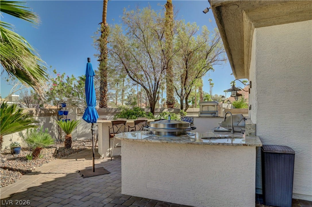 2030 Marina Bay Court, Las Vegas, NV 89117 An integrated outdoor kitchen and bar sit on the stone-paved patio under towering palm trees.