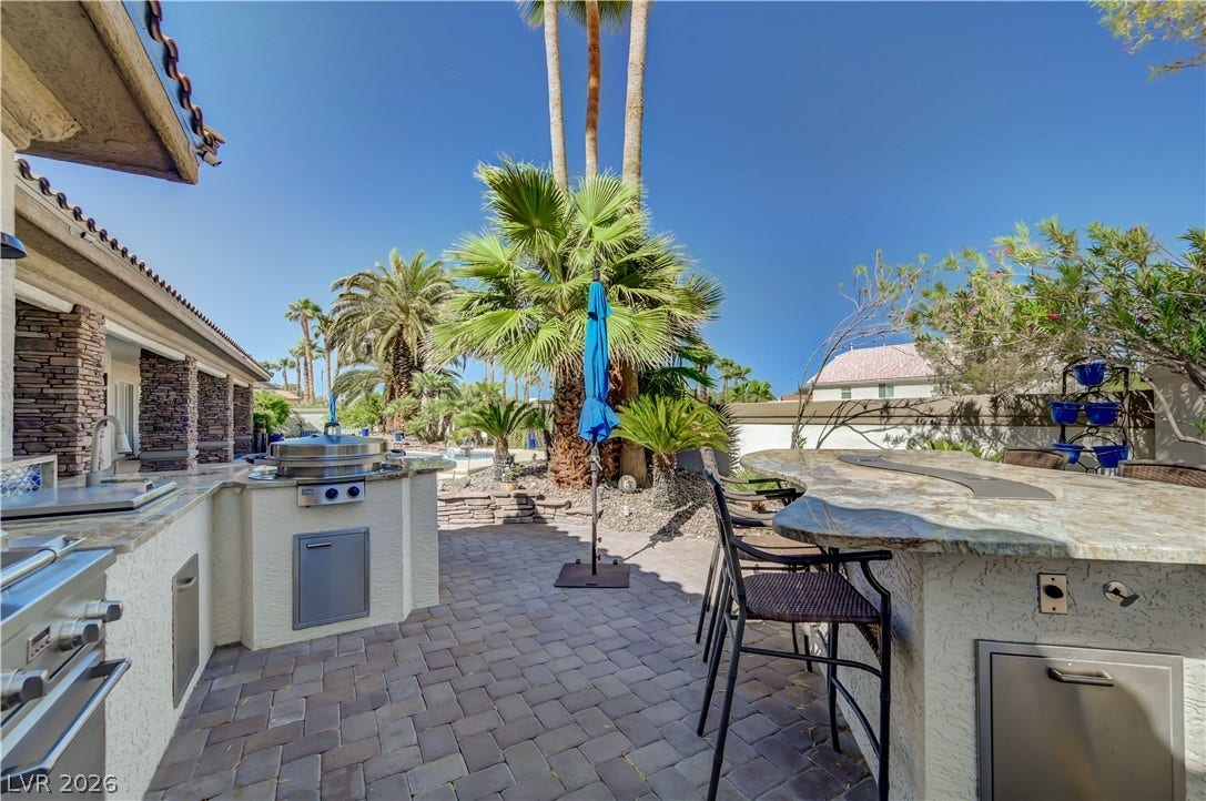 2030 Marina Bay Court, Las Vegas, NV 89117 An expansive paver patio centers around a stone-faced outdoor kitchen surrounded by mature palm trees.