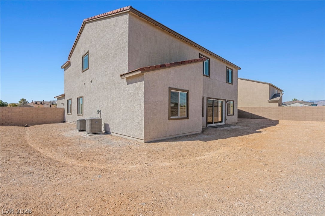 An expansive dirt backyard surrounds the rear stucco exterior of this multi-level home.