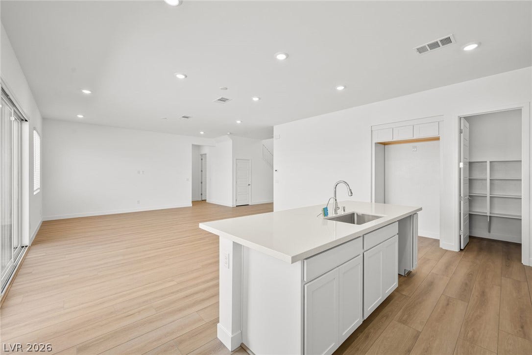 An open layout connects the kitchen island to a light-filled living area with wood floors.