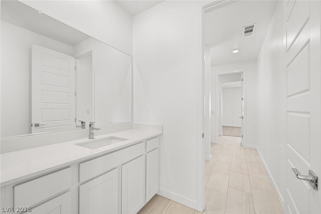 Clean lines and stone counters highlight this modern vanity area leading to a bright hallway.