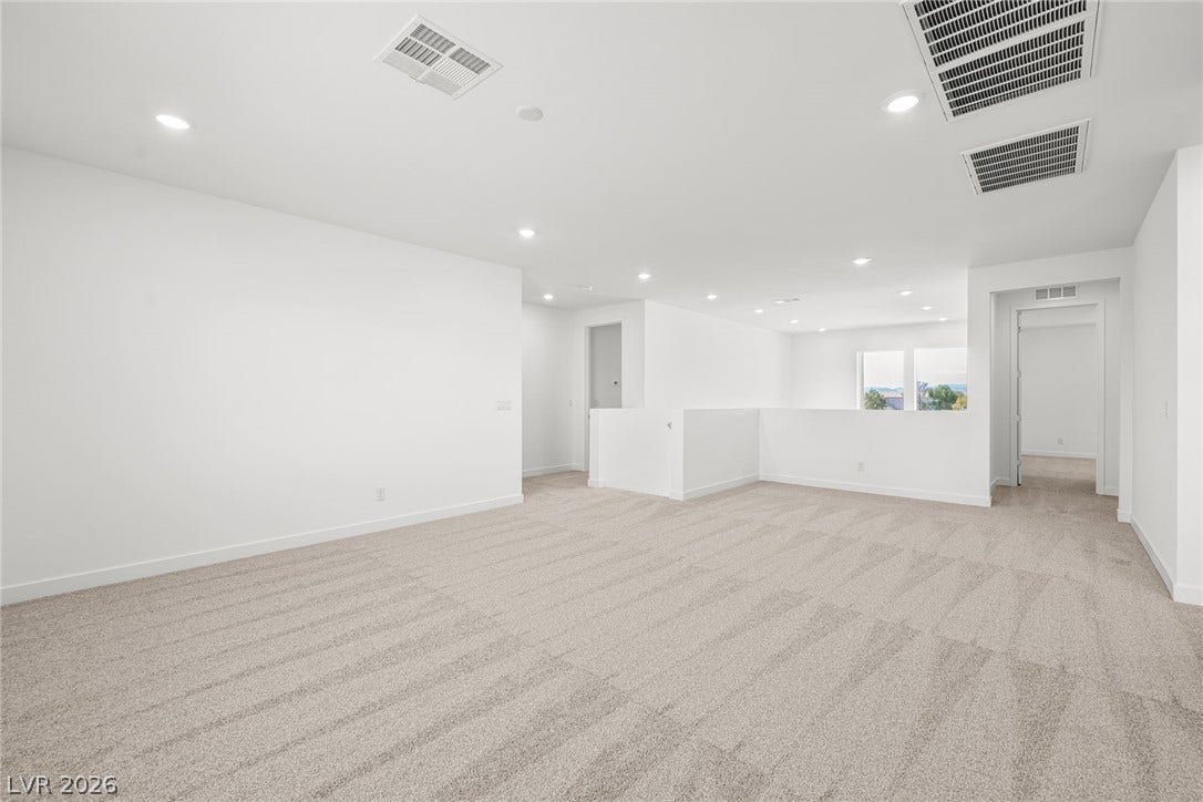 Recessed lighting illuminates a sprawling upstairs loft featuring plush carpeting and clean-lined walls.