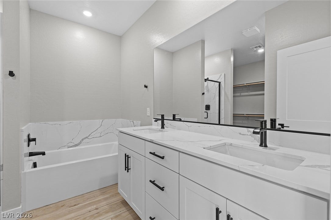 4460 Cave Lake Avenue, North Las Vegas, NV 89032 Clean lines and stone counters highlight this modern primary bathroom with a soaking tub.