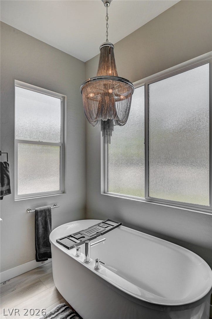 2689 Pioneer Estates Court, Las Vegas, NV 89117 An elegant soaking tub sits beneath a statement light fixture and frosted privacy windows.