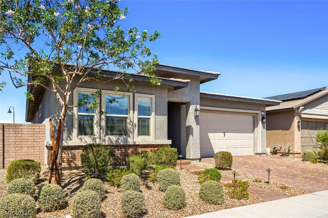 647 Longfeather Street, Henderson, NV 89011 A paved driveway leads to a modern stucco home with desert landscaping and stone accents.