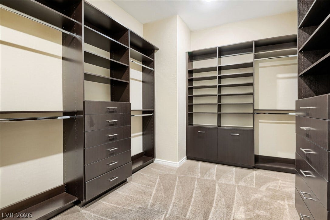 647 Longfeather Street, Henderson, NV 89011 Custom dark wood cabinetry and carpet flooring organize this spacious walk-in closet.