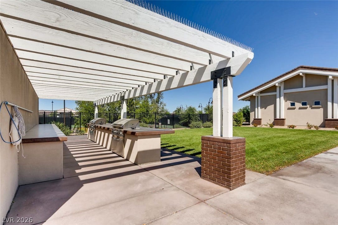 647 Longfeather Street, Henderson, NV 89011 A timber pergola shades the built-in outdoor kitchen alongside a manicured lawn area.