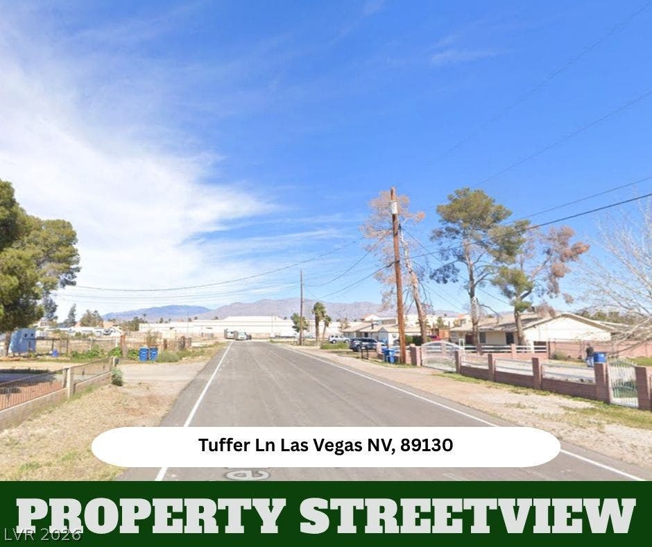 A paved neighborhood street leads toward a backdrop of distant mountains under blue skies.
