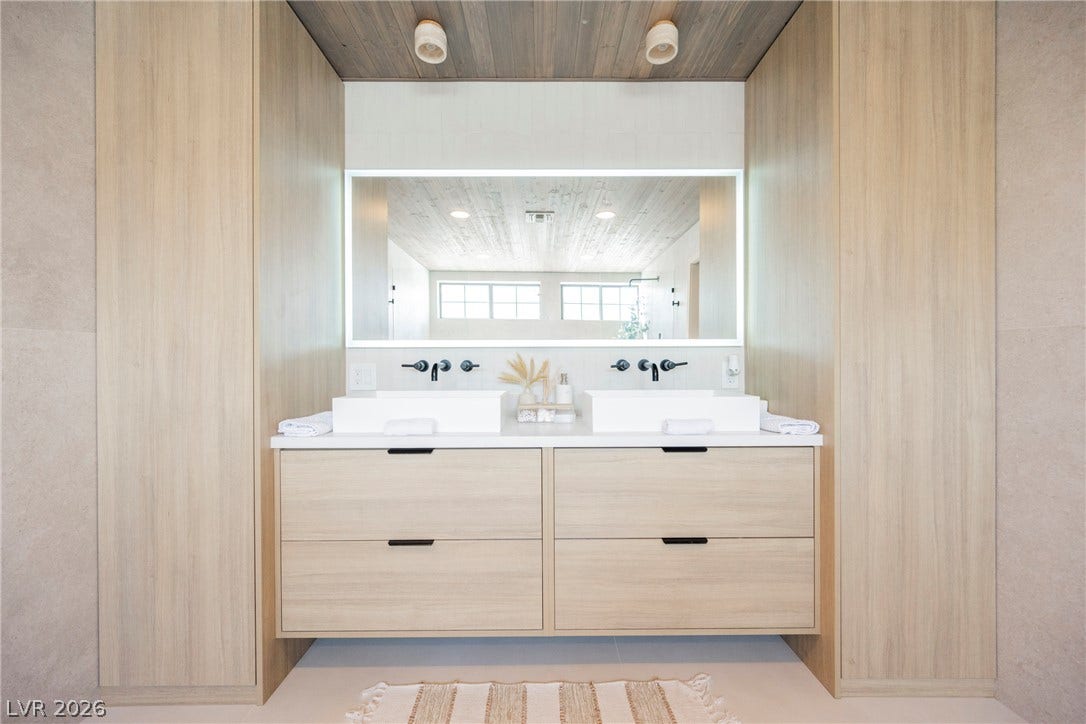 5741 S Pearl Street, Las Vegas, NV 89120 A floating light-wood vanity features dual vessel sinks beneath an illuminated mirror and planked ceiling.