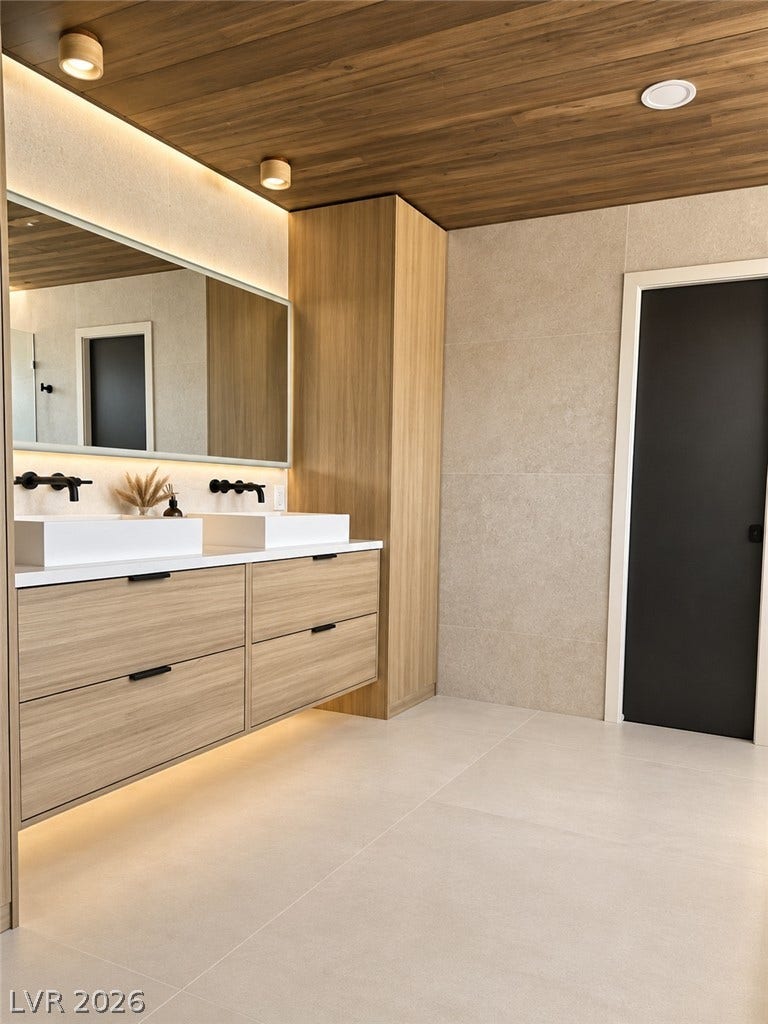 5741 S Pearl Street, Las Vegas, NV 89120 Rich wood plank ceilings and clean stone tile flooring frame a sleek modern floating vanity.