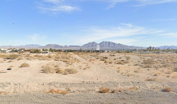 Rugged desert terrain stretches toward majestic mountain peaks under a vast blue sky.