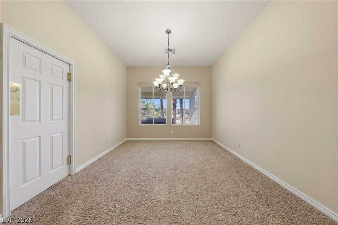 An elegant chandelier highlights this versatile dining space with soft carpeting and natural light.